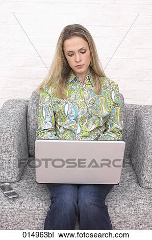 Stock Image - young woman sitting on armchair working with laptop computer. Fotosearch