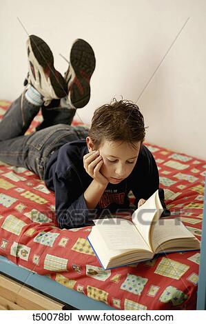 Stock Image - Boy reading book in bed. Fotosearch