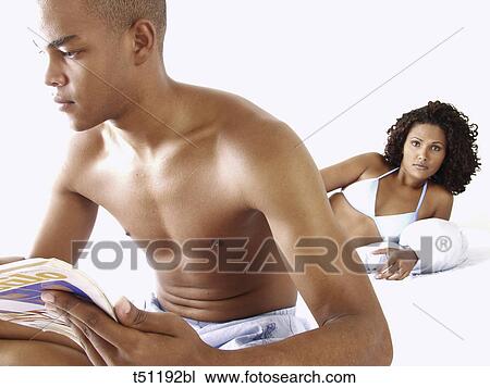 Couple on bed, woman looking at him while he's reading a magazine View Large Photo Image Stock Image - Couple on bed, woman looking at him while he's reading a magazine. Fotosearch