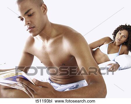 Couple on bed, woman looking at him while he's reading a magazine View Large Photo Image Stock Image - Couple on bed, woman looking at him while he's reading a magazine. Fotosearch