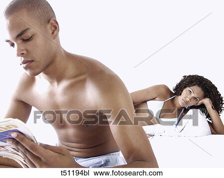 Couple on bed, woman looking at him while he's reading a magazine View Large Photo Image Stock Image - Couple on bed, woman looking at him while he's reading a magazine. Fotosearch