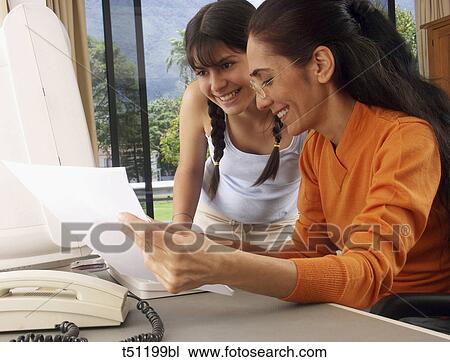 Stock Image - Daughter looking at mother while she's working at home. Fotosearch
