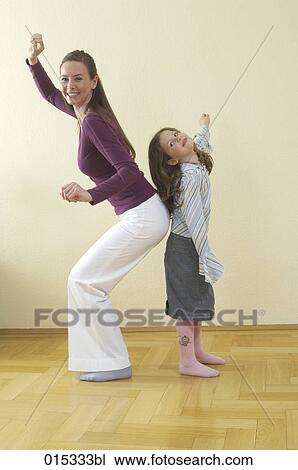 Stock Image - full body portrait of mother and young daughter standing back to back having fun. Fotosearch