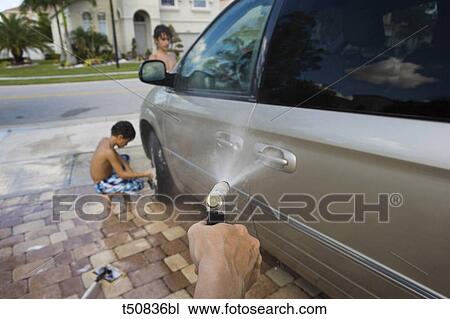 Stock Image - Hand of woman with water hose, washing car with kids in driveway of house. Fotosearch