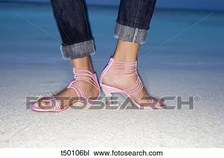 Stock Image - Low section of a woman standing on beach wearing sandals. Fotosearch
