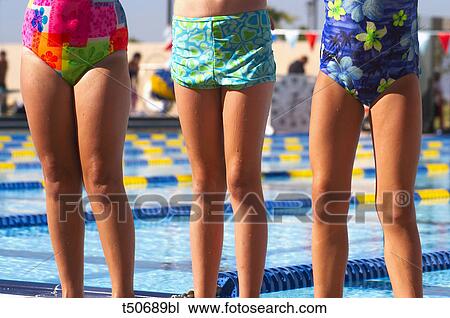Stock Image - Low section of three girls in swimsuit at swimming pool. Fotosearch