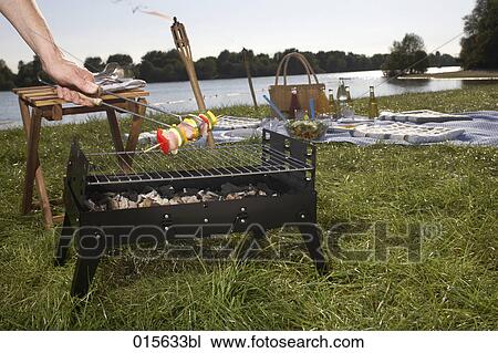 Stock Image - male hand holding barbecue tongs taking shashlik from charcoal grill. Fotosearch