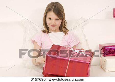 Stock Image - portrait of girl sitting on sofa holding presents. Fotosearch