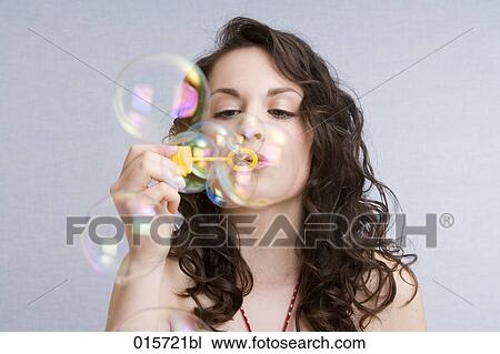 Stock Image - portrait of young woman blowing soap bubbles. Fotosearch