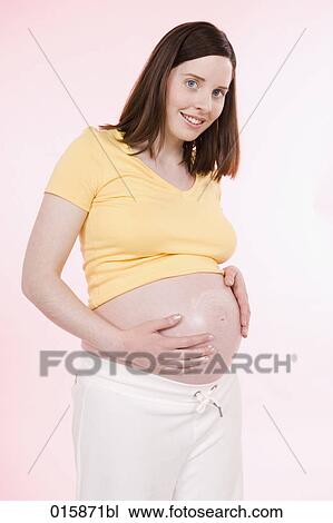 Stock Image - pregnant young woman applying lotion on her belly to avoid stretch marks. Fotosearch
