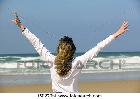 Rear view of a woman with arms raised at the beach View Large Photo Image Stock Image - Rear view of a woman with arms raised at the beach. Fotosearch