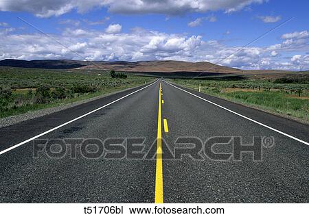 Stock Image - road with yellow strip heading off to the distant mountains in the Western United States. Fotosearch