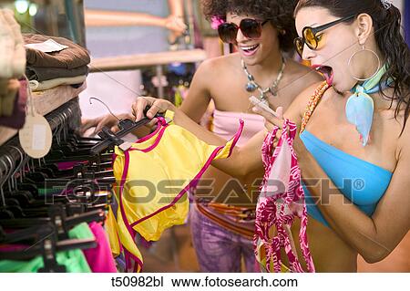 Surprised woman in a clothes shop with a friend reading tag on swimsuit View Large Photo Image Stock Image - Surprised woman in a clothes shop with a friend reading tag on swimsuit. Fotosearch