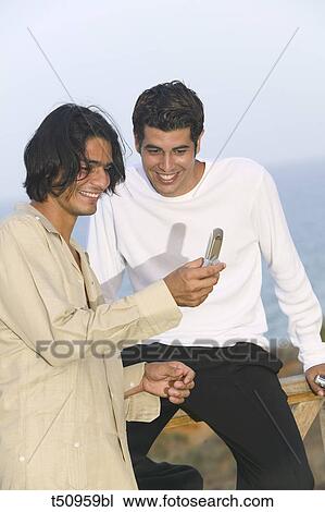 Two male friends looking at mobile phone View Large Photo Image Stock Image - Two male friends looking at mobile phone. Fotosearch