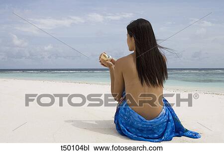 Woman sitting on beach holding a shell View Large Photo Image Stock Image - Woman sitting on beach holding a shell. Fotosearch