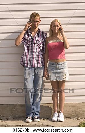 full body portrait of young couple standing against wall using mobile phones View Large Photo Image Stock Image - full body portrait of young couple standing against wall using mobile phones. Fotosearch