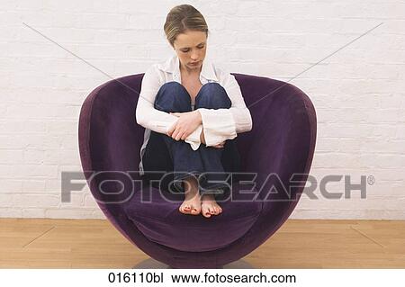 Stock Image - full body portrait of young woman sitting purple chair looking depressed. Fotosearch