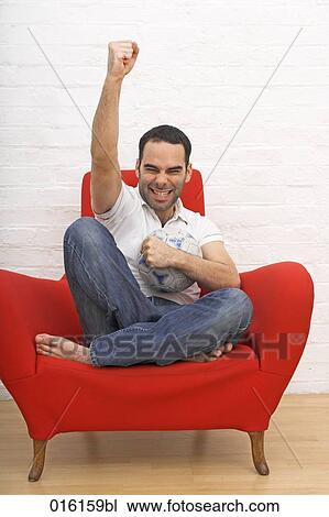 joyous young man sitting in red arm chair holding football View Large Photo Image Stock Image - joyous young man sitting in red arm chair holding football. Fotosearch