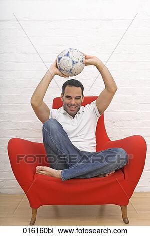 joyous young man sitting in red arm chair holding football View Large Photo Image Stock Image - joyous young man sitting in red arm chair holding football. Fotosearch