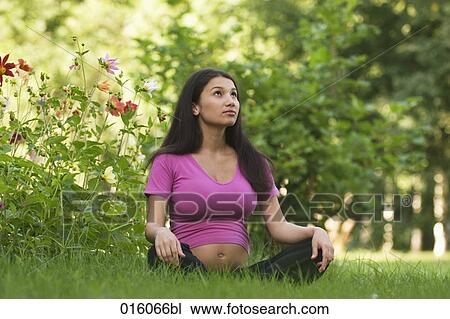 Stock Image - portrait of pregnant young woman sitting on meadow in park. Fotosearch