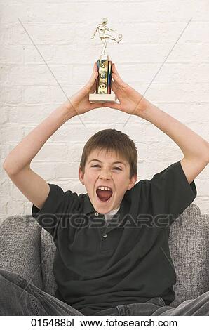 Stock Image - portrait of young boy celebrating with football trophy. Fotosearch