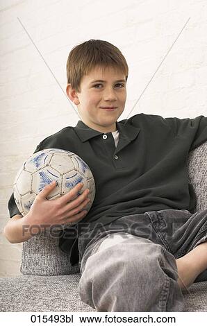 portrait of young boy sitting in arm chair holding football View Large Photo Image Stock Image - portrait of young boy sitting in arm chair holding football. Fotosearch