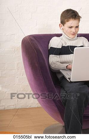 portrait of young boy sitting in arm chair with earphones and laptop computer View Large Photo Image Stock Image - portrait of young boy sitting in arm chair with earphones and laptop computer. Fotosearch