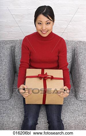 Stock Image - portrait of young japanese woman sitting in arm chair holding present. Fotosearch