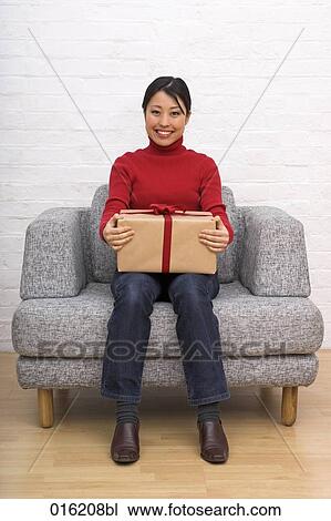 Stock Image - portrait of young japanese woman sitting in arm chair holding present. Fotosearch