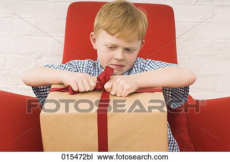 Stock Image - red haired boy trying to open present. Fotosearch