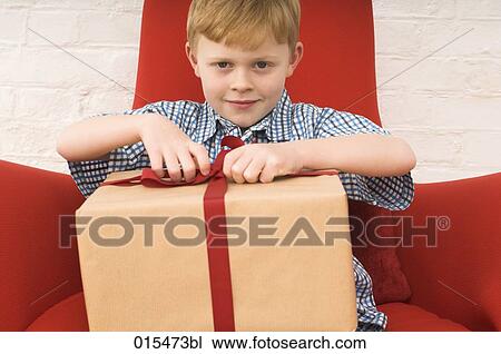 Stock Image - red haired boy trying to open present. Fotosearch
