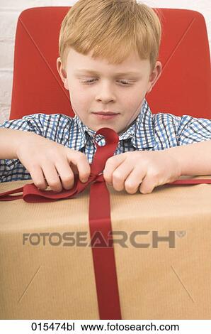 Stock Image - red haired boy trying to open present. Fotosearch