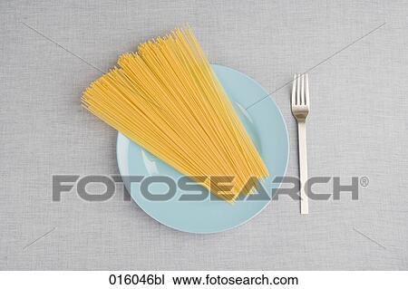 Stock Image - still life of raw spaghetti on blue plate with fork. Fotosearch