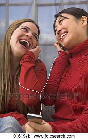 Stock Image - two young woman listening to music sharing earphones. Fotosearch
