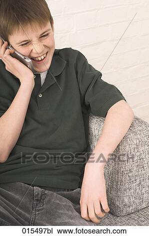 Stock Image - young boy sitting in arm chair talking on mobile phone. Fotosearch