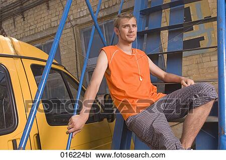 young man in orange t-shirt sitting on stairs listening to music on mp3 player View Large Photo Image Stock Image - young man in orange t-shirt sitting on stairs listening to music on mp3 player. Fotosearch