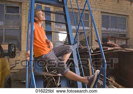 Stock Image - young man in orange t-shirt sitting on stairs listening to music on mp3 player. Fotosearch