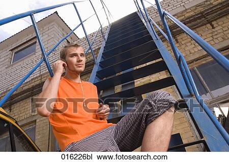 young man in orange t-shirt sitting on stairs listening to music on mp3 player View Large Photo Image Stock Image - young man in orange t-shirt sitting on stairs listening to music on mp3 player. Fotosearch