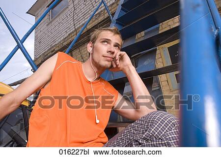 young man in orange t-shirt sitting on stairs listening to music on mp3 player View Large Photo Image Stock Image - young man in orange t-shirt sitting on stairs listening to music on mp3 player. Fotosearch