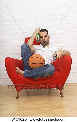 young man sitting in red arm chair holding basketball and beer bottle while watching tv View Large Photo Image Stock Image - young man sitting in red arm chair holding basketball and beer bottle while watching tv. Fotosearch