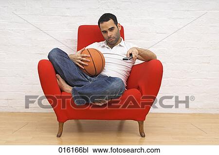 young man sitting in red arm chair holding basketball while watching tv View Large Photo Image Stock Image - young man sitting in red arm chair holding basketball while watching tv. Fotosearch