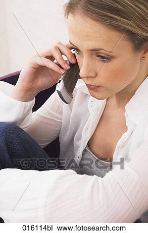 Stock Image - young woman sitting in arm chair talking on mobile phone. Fotosearch