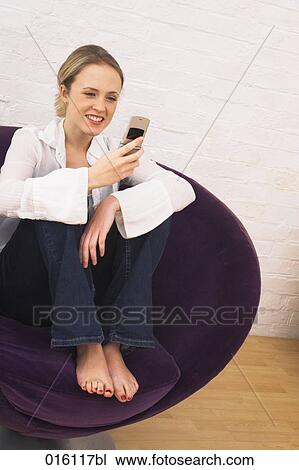 young woman sitting in arm chair checking her mobile phone for text messages View Large Photo Image Stock Image - young woman sitting in arm chair checking her mobile phone for text messages. Fotosearch