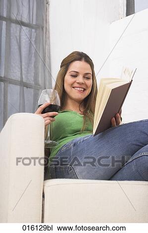 young woman sitting in arm chair reading book and drinking glass of red wine View Large Photo Image Stock Image - young woman sitting in arm chair reading book and drinking glass of red wine. Fotosearch