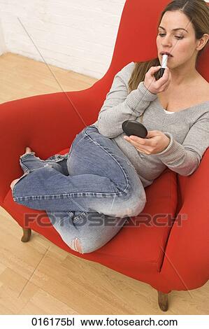 young woman sitting in arm chair applying lipstick View Large Photo Image Stock Image - young woman sitting in arm chair applying lipstick. Fotosearch