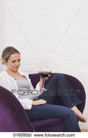 Stock Image - young woman sitting in purple arm chair holding glass of red wine. Fotosearch