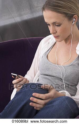 young woman sitting on arm chair listening to music on mp3 player View Large Photo Image Stock Image - young woman sitting on arm chair listening to music on mp3 player. Fotosearch