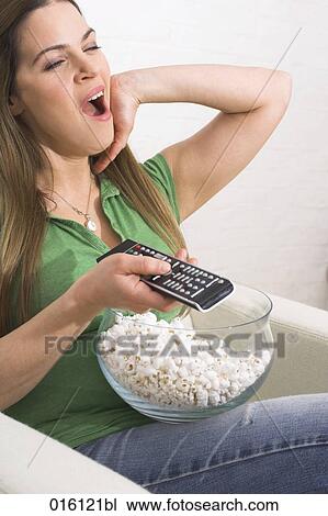 young woman watching tv holding remote control and eating popcorn View Large Photo Image Stock Image - young woman watching tv holding remote control and eating popcorn. Fotosearch