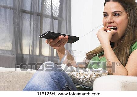 young woman watching tv holding remote control and eating popcorn View Large Photo Image Stock Image - young woman watching tv holding remote control and eating popcorn. Fotosearch