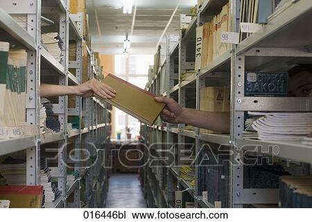 Stock Image - book being transferred from one student to another through shelf in school library. Fotosearch